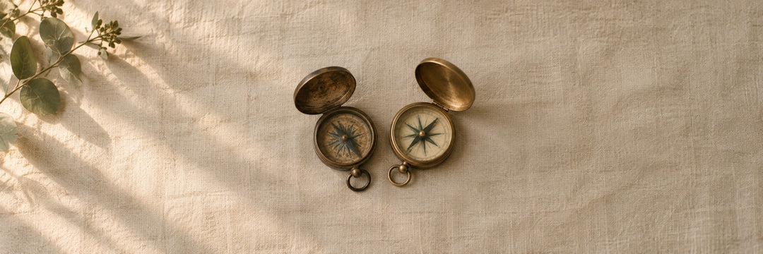 Two brass pocket compasses side by side on pale linen, one older than the other