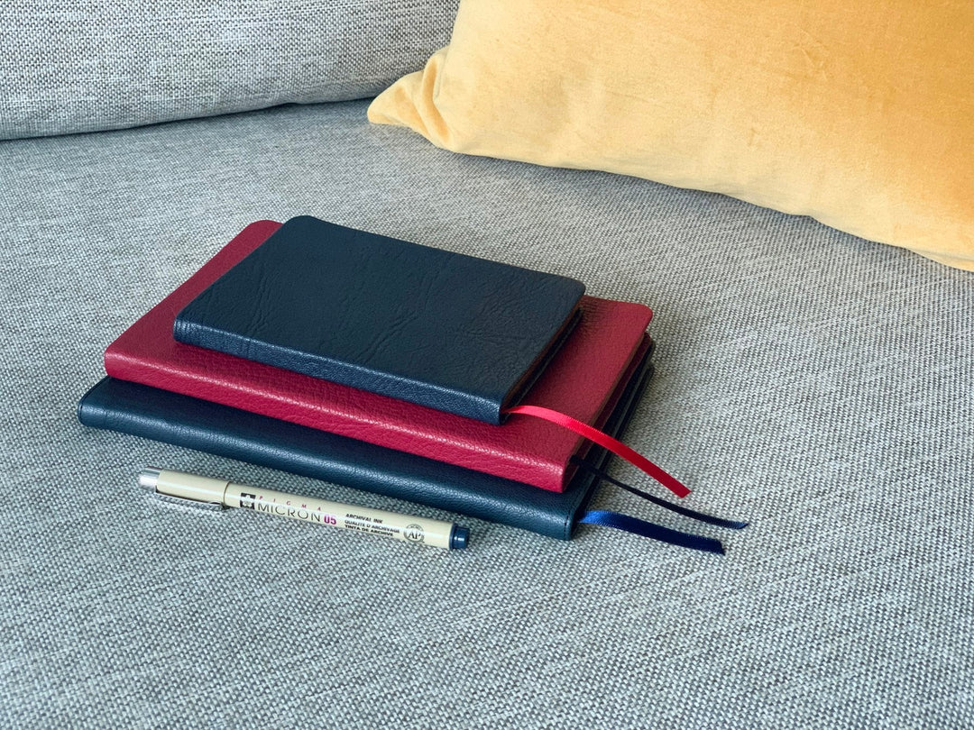 A small stack of leather journals with a pen