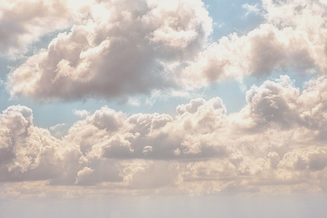 Soft cream and pink clouds drifting across a pale blue sky