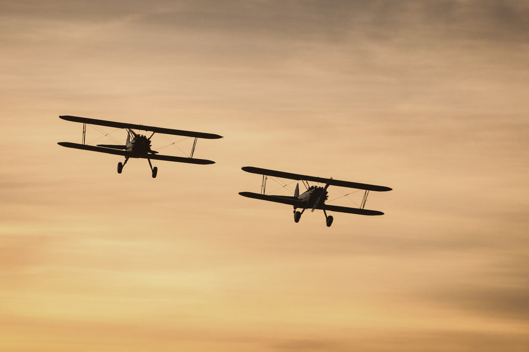 Two vintage biplanes flying against an amber sky