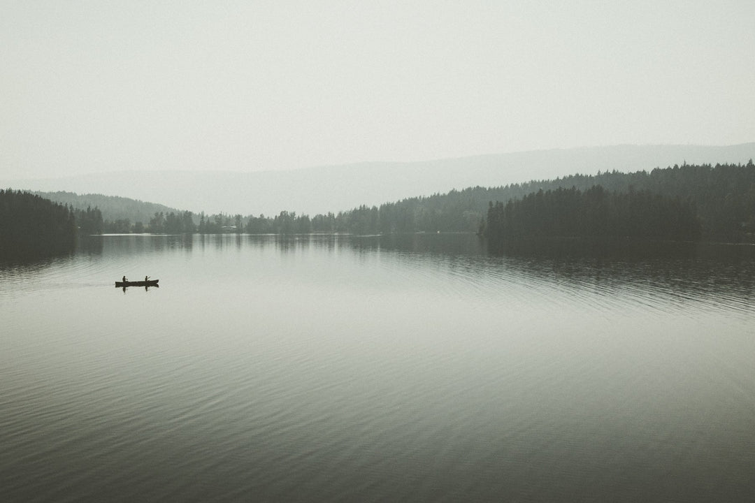 A misty lake with a single small boat far in the distance
