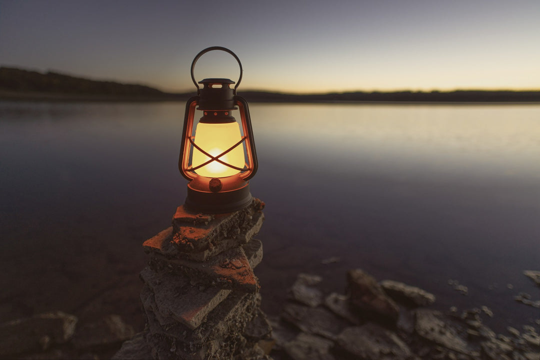 A glowing lantern on the rocks beside a still lake at dusk