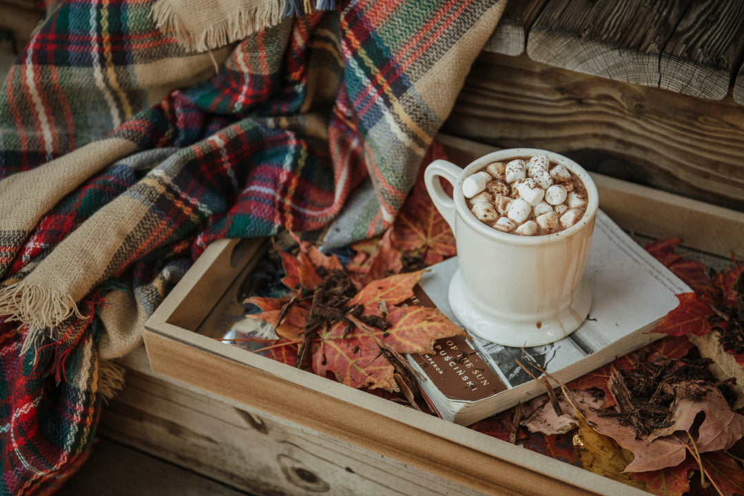 A white mug of hot chocolate resting on a book on a cozy autumn day