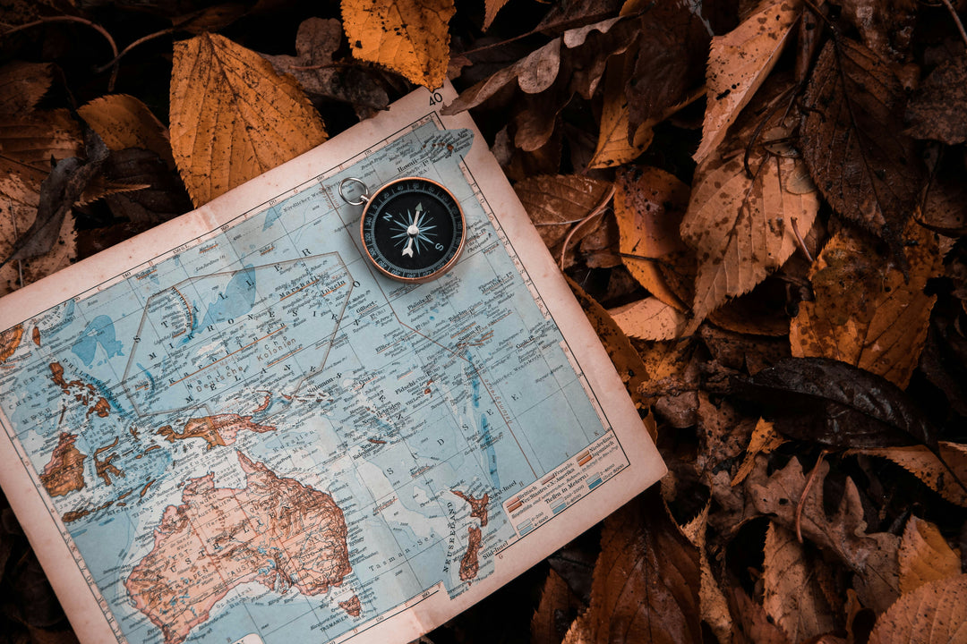An old compass resting on a folded paper map on a bed of dry autumn leaves