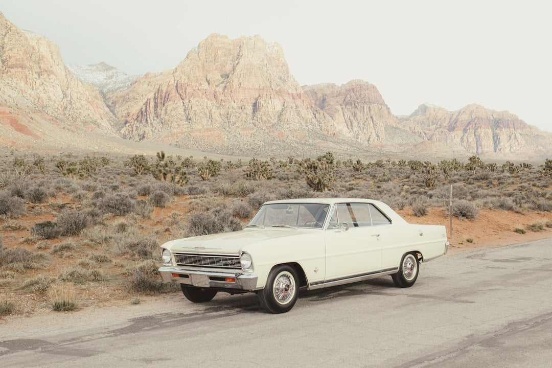 A classic cream car parked on a desert road beneath red rock mountains