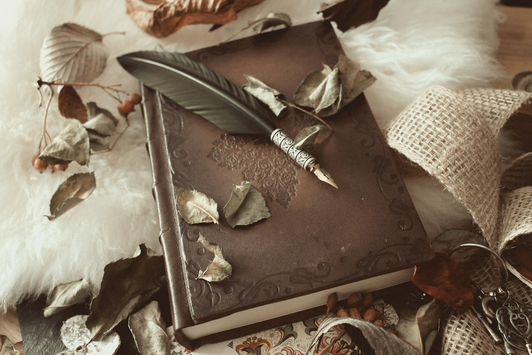 An antique leather journal with a quill and dried flowers