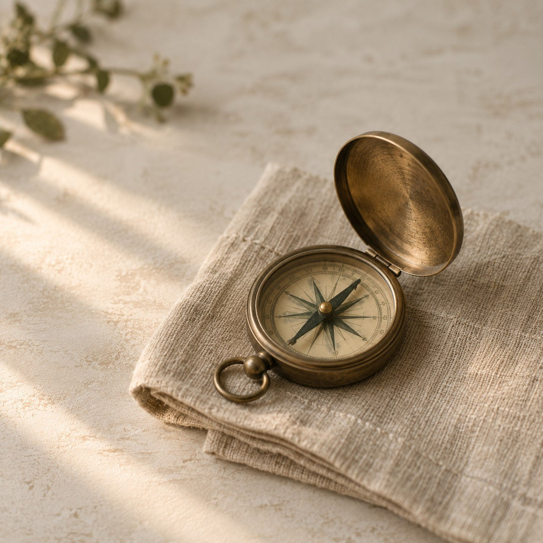 An open brass pocket compass resting on folded linen in warm afternoon light